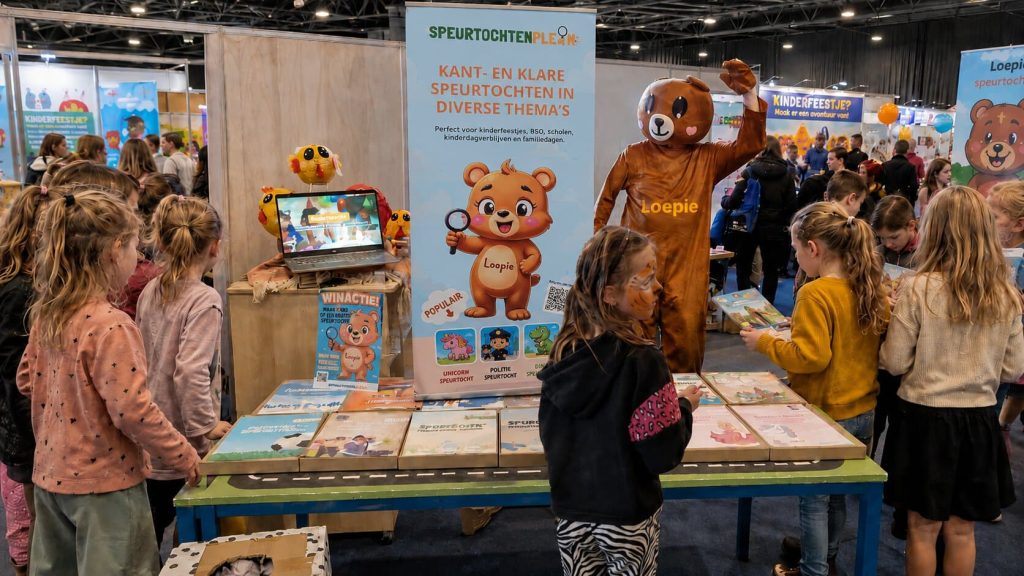 Onze kraam op de kinderbeurs, met mascotte Loepie en kinderen die de speurtochten bekijken.